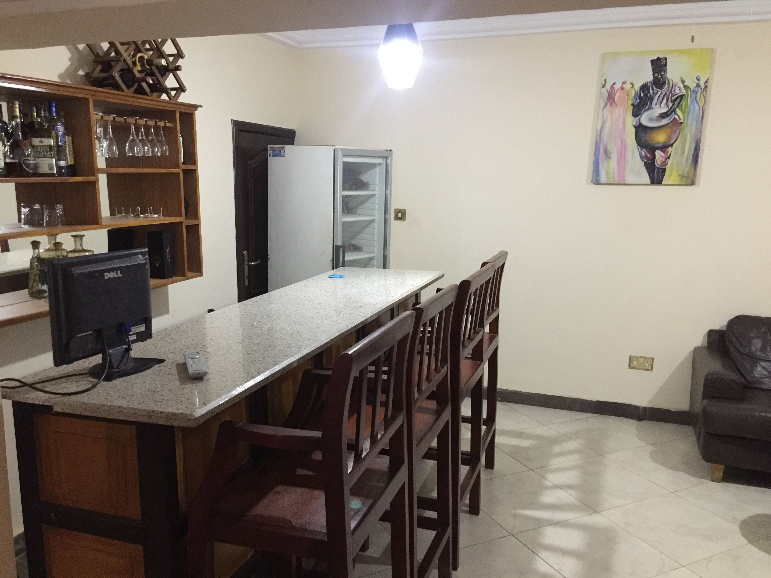A kitchen with a bar area, wooden chairs, a refrigerator, and a painting on the wall.