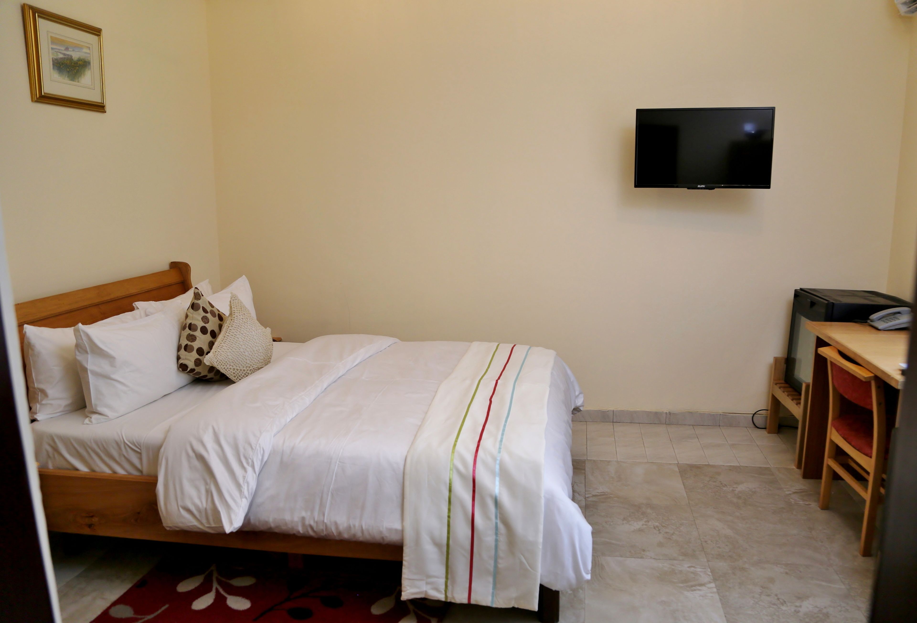 A bedroom with a bed, a television mounted on the wall, and a desk with a chair.