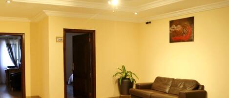 A hotel lobby with a brown leather sofa, a potted plant, a ceiling fan, and a painting on the wall.