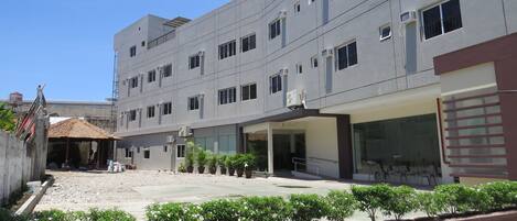 Un edificio de varios pisos con fachada plana, unidades de aire acondicionado y un área cubierta con plantas en macetas.