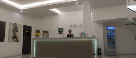 Zona de recepción de hotel con diseño moderno, una mesa de recepción, una máquina expendedora y una escalera.