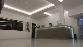 A modern reception area with a clean, minimalist design, featuring a reception desk, a wall-mounted artwork, and a refrigerator with a beverage dispenser.