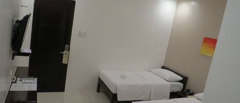 Habitación de hotel con dos camas individuales, un escritorio con silla, una mesita y una puerta que da a otra habitación.
