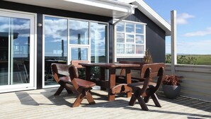 Eine Holzterrasse mit Tisch und Stühlen, große Schiebeglastüren und Blick auf die Landschaft.