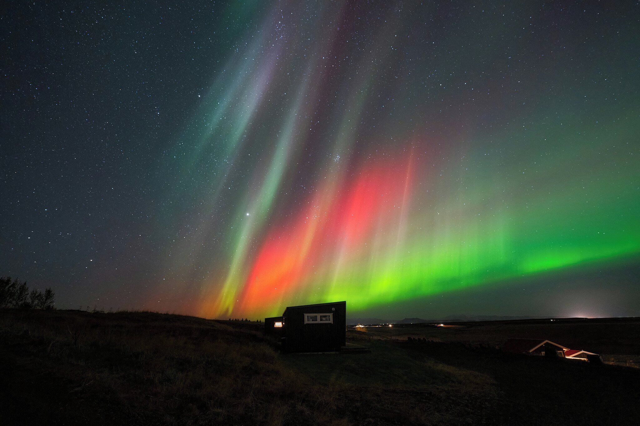 A remote cabin under a starry night sky with the aurora borealis.