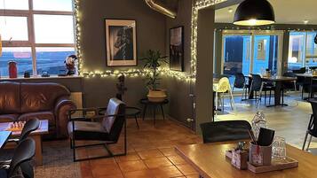 Una zona de estar acogedora con chimenea, una mesa de comedor y un sofá. Hay un ventanal con vistas, y la habitación tiene vigas de madera en el techo.