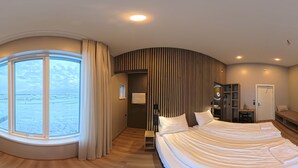 A modern hotel room with a large curved window offering a view of a snowy landscape, a curved bed, a small desk, and a seating area with a view of the room. - Hestheimar (Selfoss)