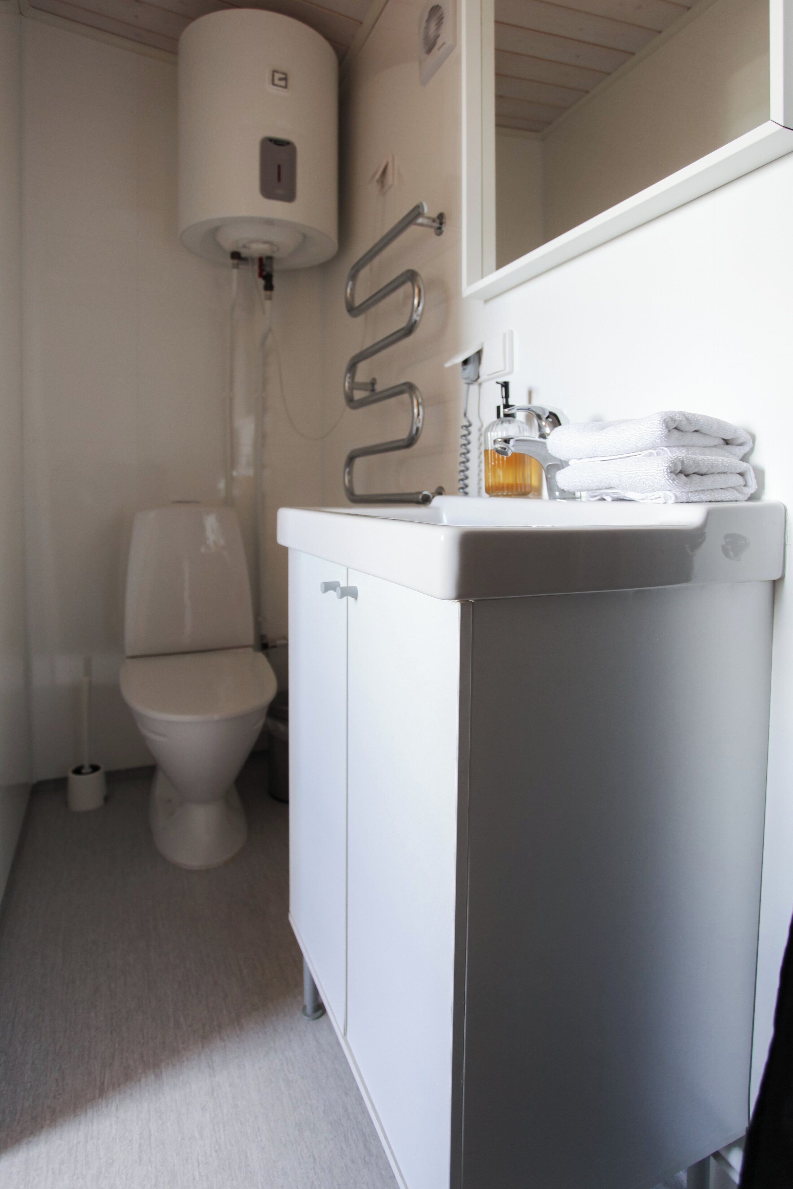 Un baño con inodoro, lavabo y dispensador de jabón, y un perchero para toallas.