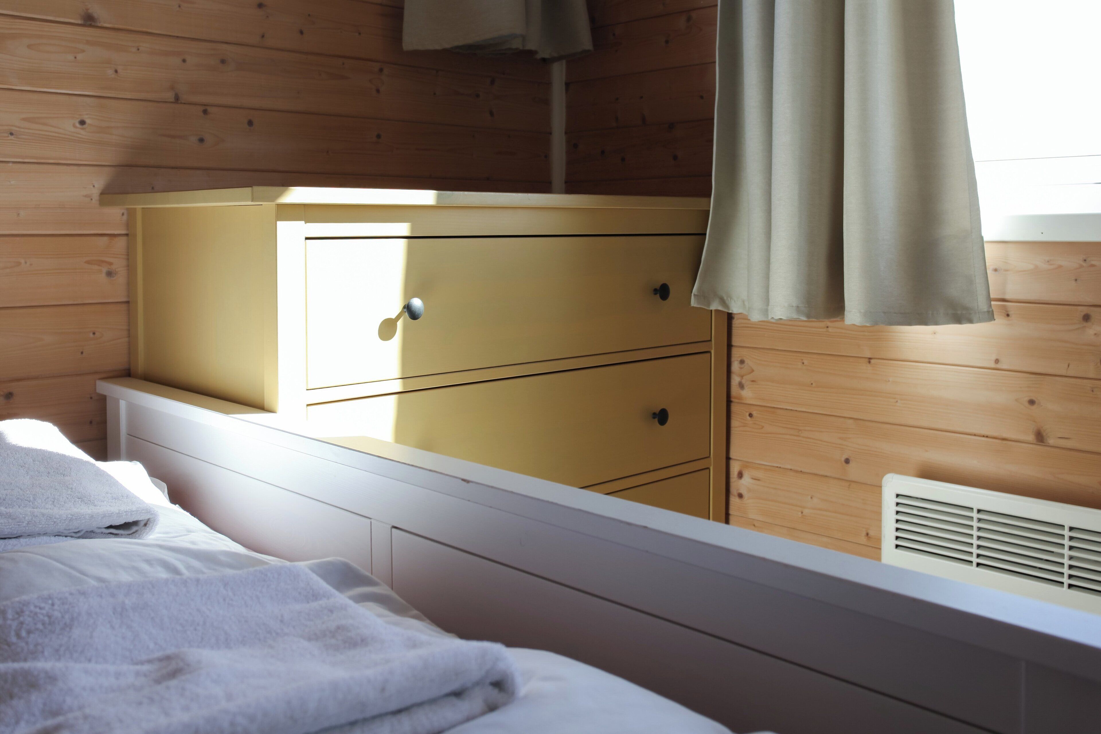 A wooden-paneled room with a bed, a yellow dresser, and a window with curtains.