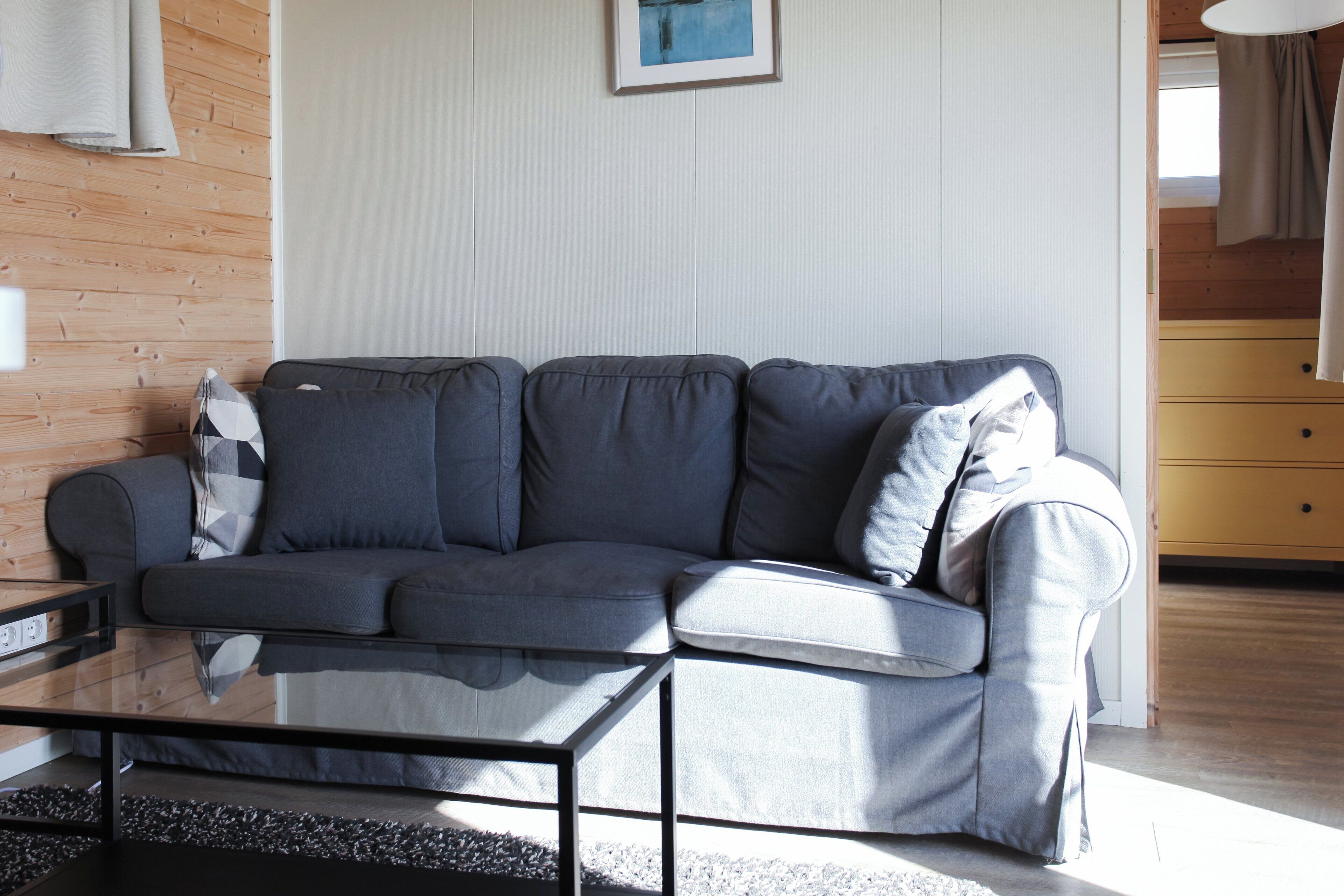 A modern living room with a grey sofa, a glass coffee table, and a wooden wall.