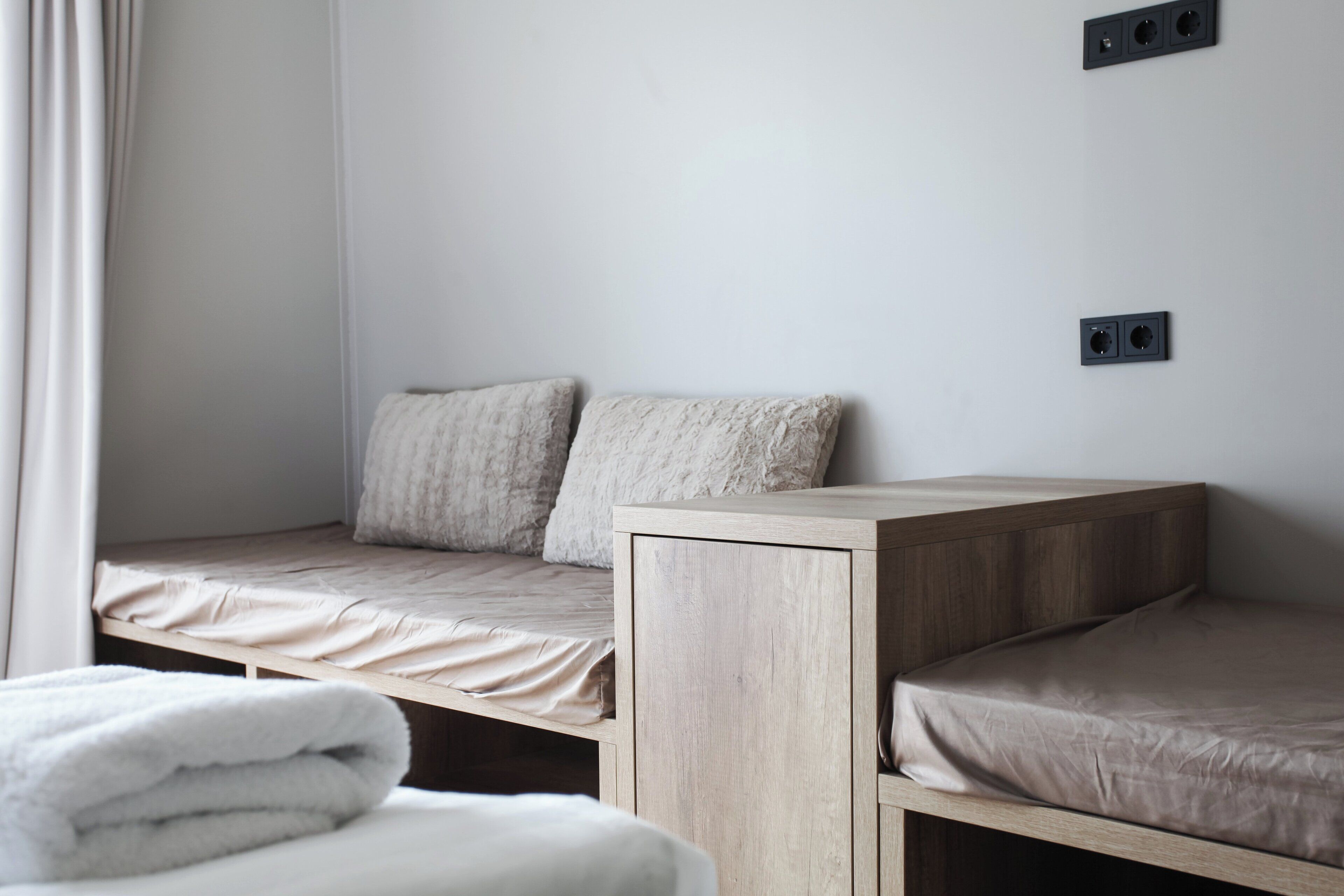 A minimalist bedroom with two beds, a wooden headboard, and a white curtain.