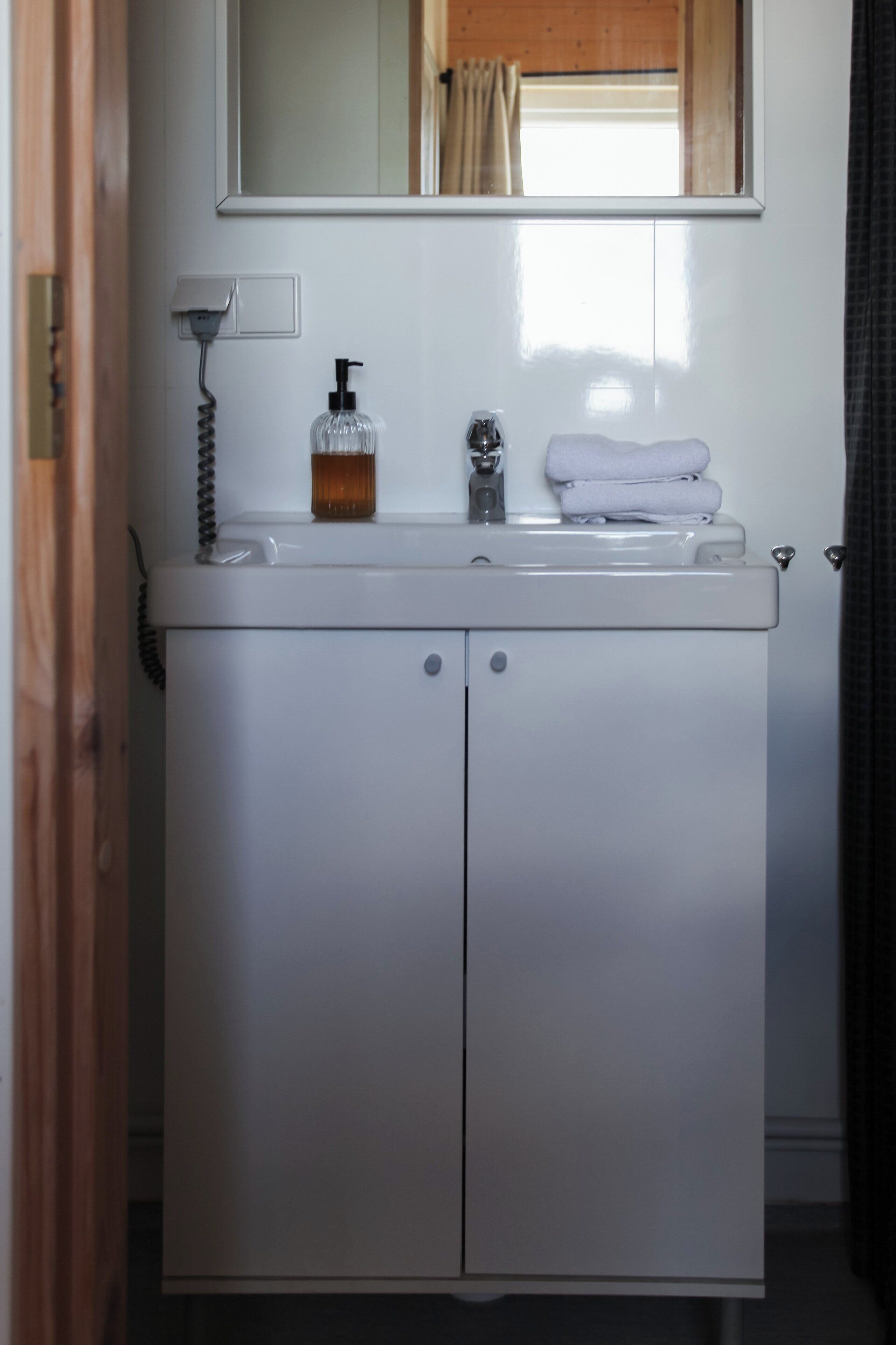 A white bathroom vanity with a mirror above the sink, a soap dispenser, and a towel stack.