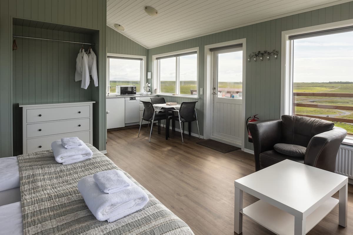 Quarto com cama, mesa, cadeira, escrivaninha com computador e vista para o exterior.
