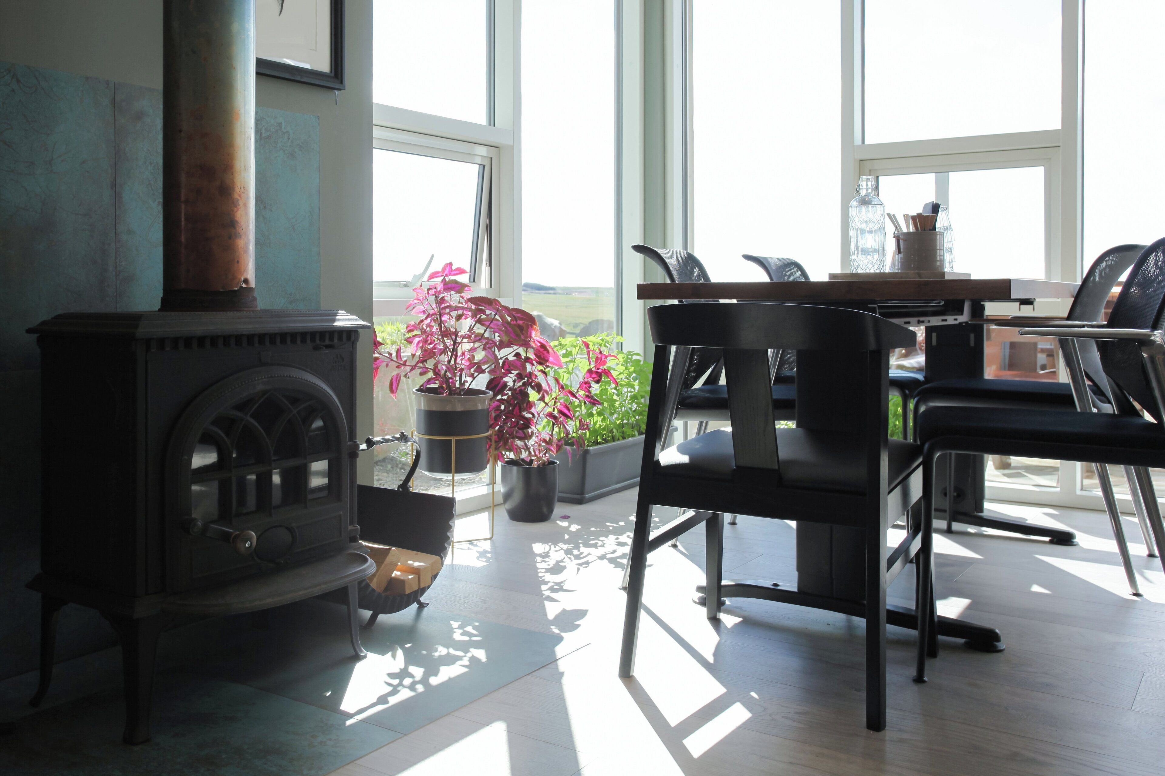 A modern living room with a wood-burning stove, black chairs, a dining table, and large windows offering a view of the outdoors.