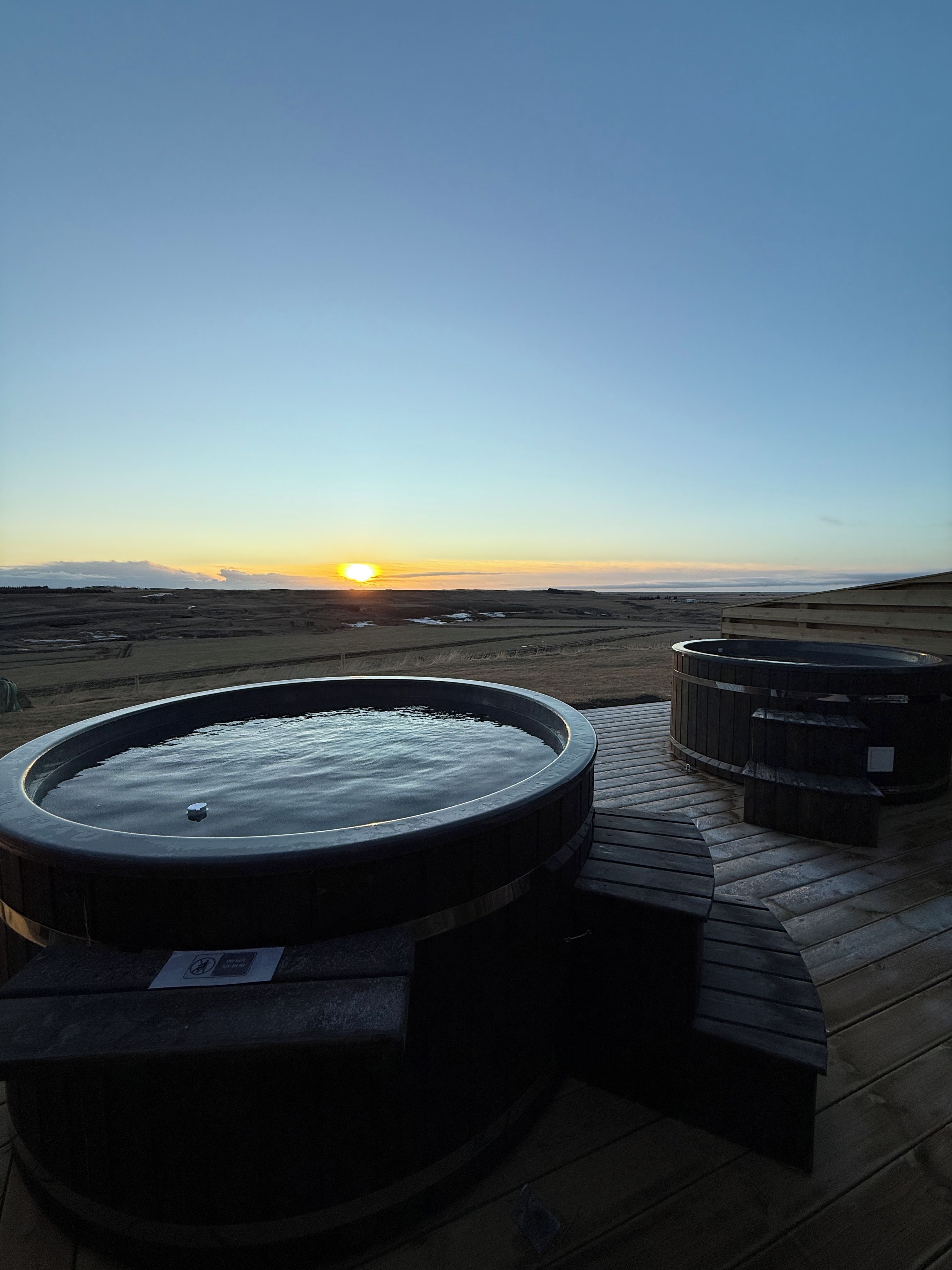 A hot tub and seating area on a deck overlooking a landscape with a sunset in the distance.