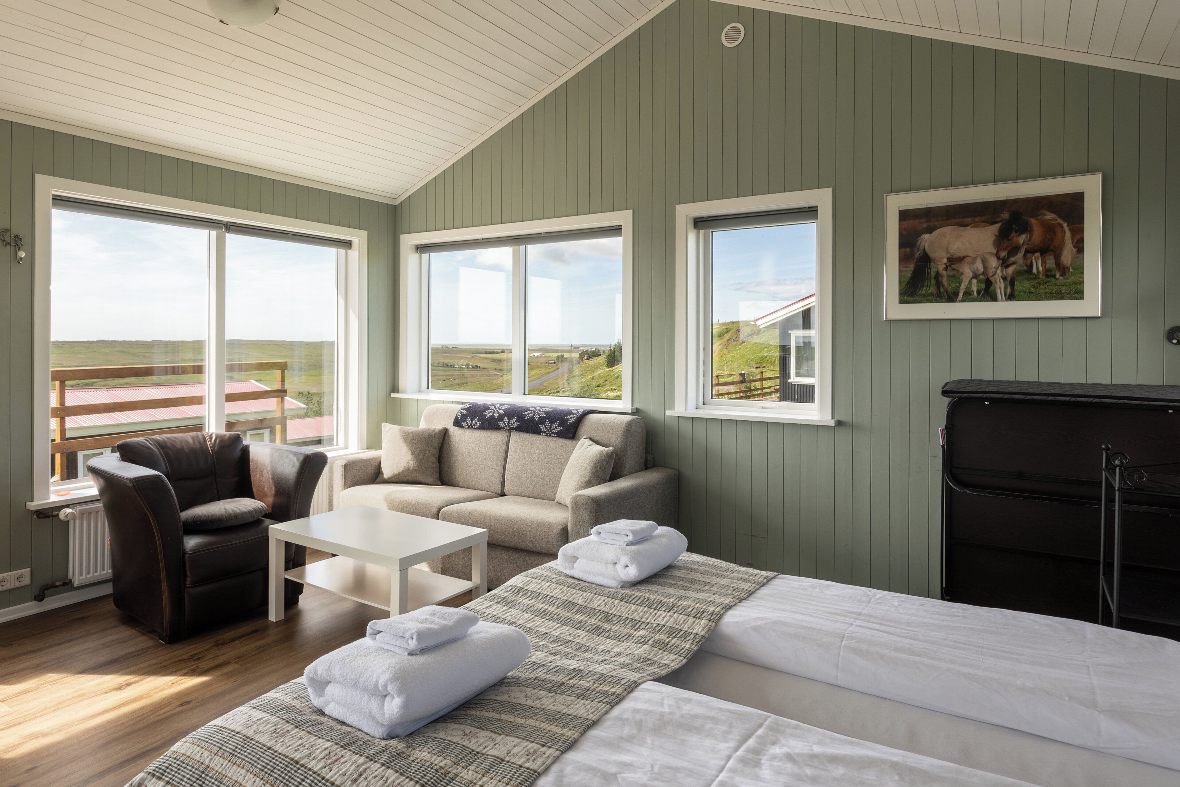 Una habitación con una cama, dos sofás, una mesa de centro y una chimenea. Amplias ventanas ofrecen vistas al exterior.
