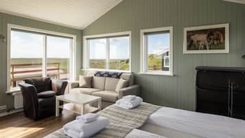 Una habitación con una cama, dos sofás, una mesa de centro y una chimenea. Amplias ventanas ofrecen vistas al exterior.