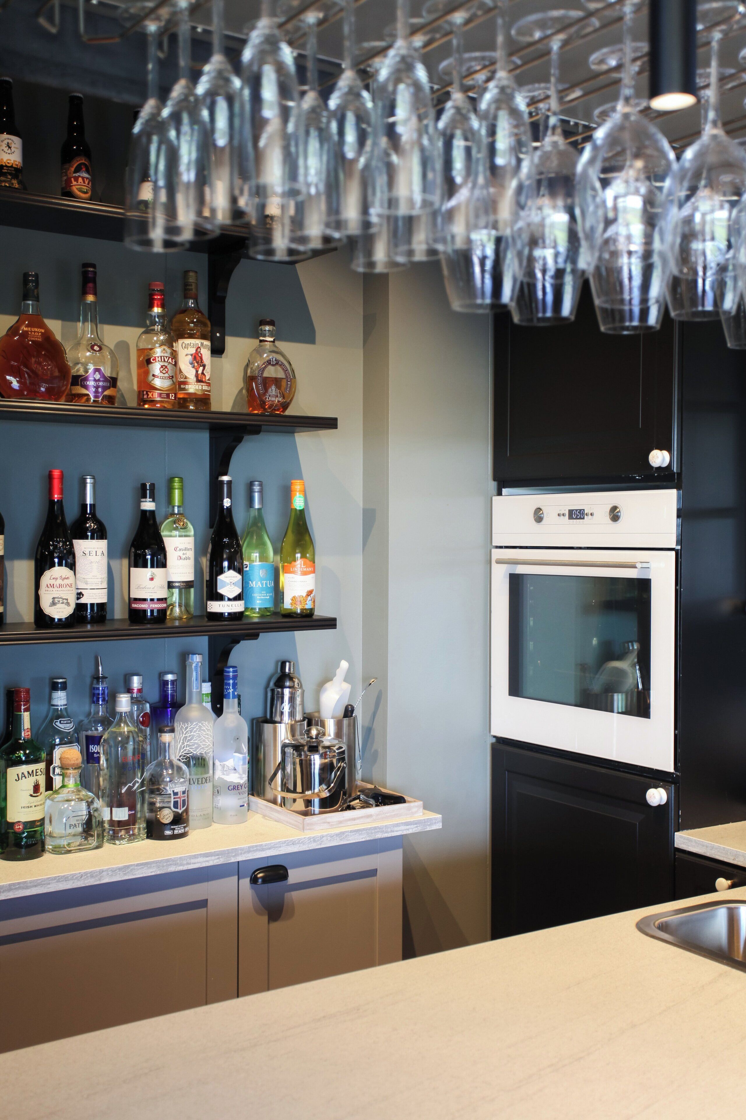 Una cocina con estantes llenos de botellas de licor, una cava de vinos y un horno empotrado.