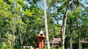 A garden with a unique red sculpture, surrounded by lush greenery and trees. - Traumvilla Bentota (Bentota)