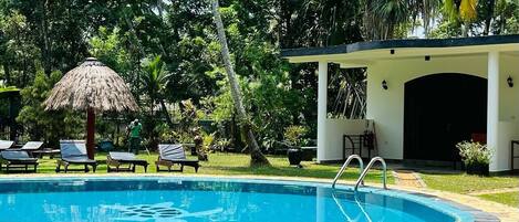 A swimming pool with lounge chairs, a thatched umbrella, and a covered area with a door.