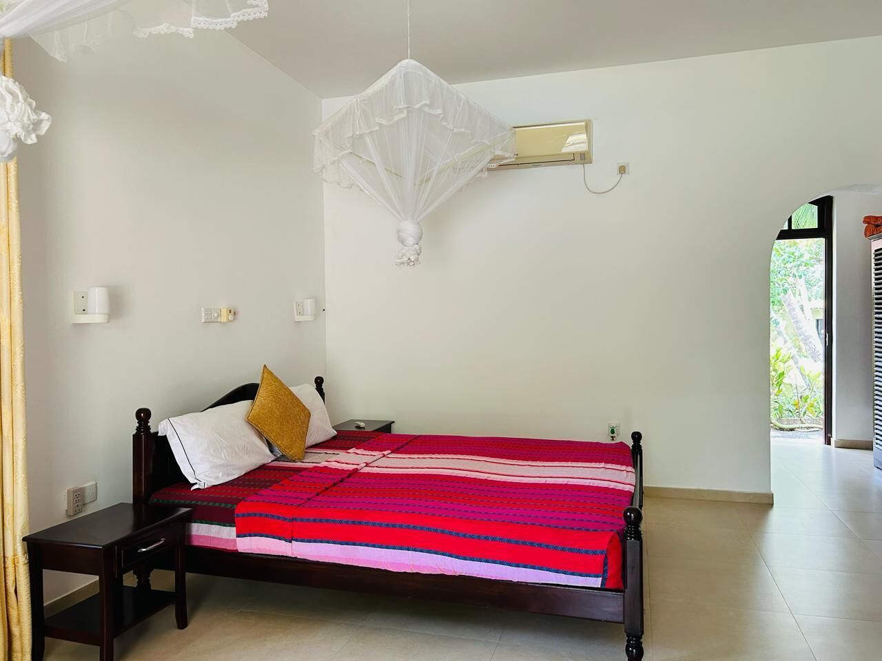 A bedroom with a bed, bedside table, and a hanging mosquito net.