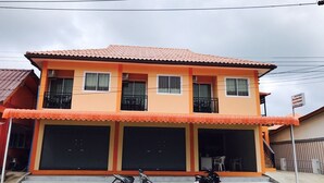 Um edifício de dois andares com telhado de telhas vermelhas, duas varandas e uma placa indicando ser um complexo de apartamentos.