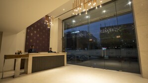A reception desk with a modern design, a large glass window, and a view of a hospital building. - Grand Continent Secunderabad A Sarovar Portico Affiliate Hotel (Hyderabad)