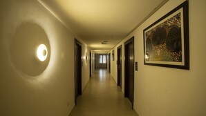 A hotel hallway with a circular light fixture on the left, a framed artwork on the right, and doors leading to rooms. - Grand Continent Secunderabad A Sarovar Portico Affiliate Hotel (Hyderabad)