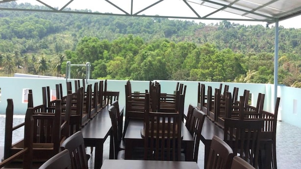 A covered outdoor dining area with tables and chairs, overlooking a lush green landscape. - Huy Hoang Hotel (Phu Quoc)