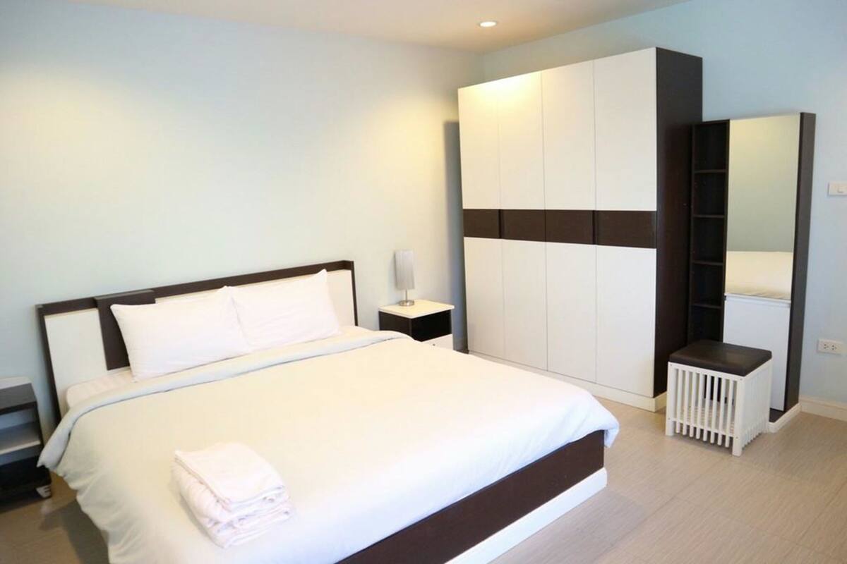 A modern hotel room with a large bed, a wardrobe, a small stool, and a nightstand.