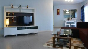 A modern living room with a flat-screen TV on a white entertainment unit, a glass coffee table, a red sofa, and a dining area with white chairs. - 999 Triple Nine Boutique Hotel (Hua Hin)
