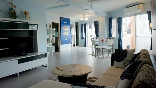 A modern living room with a flat-screen TV, a round coffee table, and a sofa. There is a dining area with a table and chairs in the background. - 999 Triple Nine Boutique Hotel (Hua Hin)