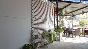 An outdoor seating area with tables and chairs, a white wall with horizontal slats, and a covered section with a metal roof. - 999 Triple Nine Boutique Hotel (Hua Hin)