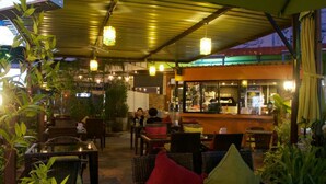 An outdoor seating area with wicker furniture and cushions, a bar in the background, and potted plants. - 999 Triple Nine Boutique Hotel (Hua Hin)