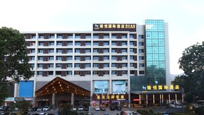 Um hotel com vários andares, uma entrada imponente e um edifício moderno em vidro ao lado.