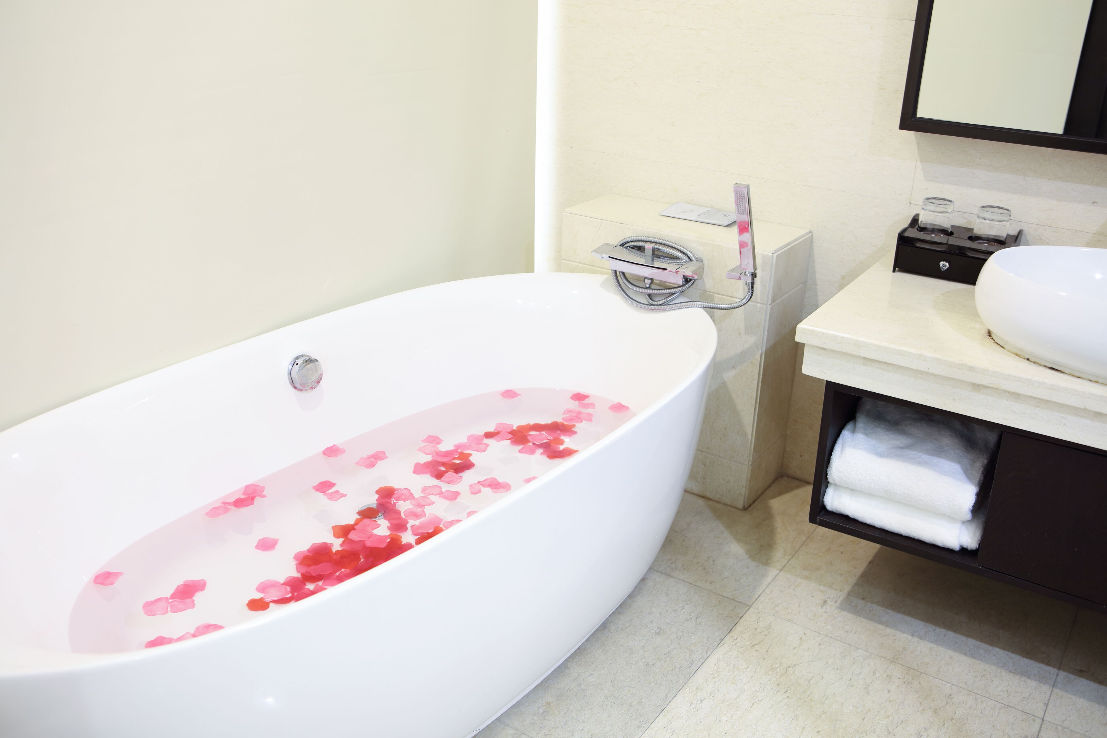 Un baño moderno con una bañera independiente llena de pétalos de rosa, un lavamanos blanco y un perchero.