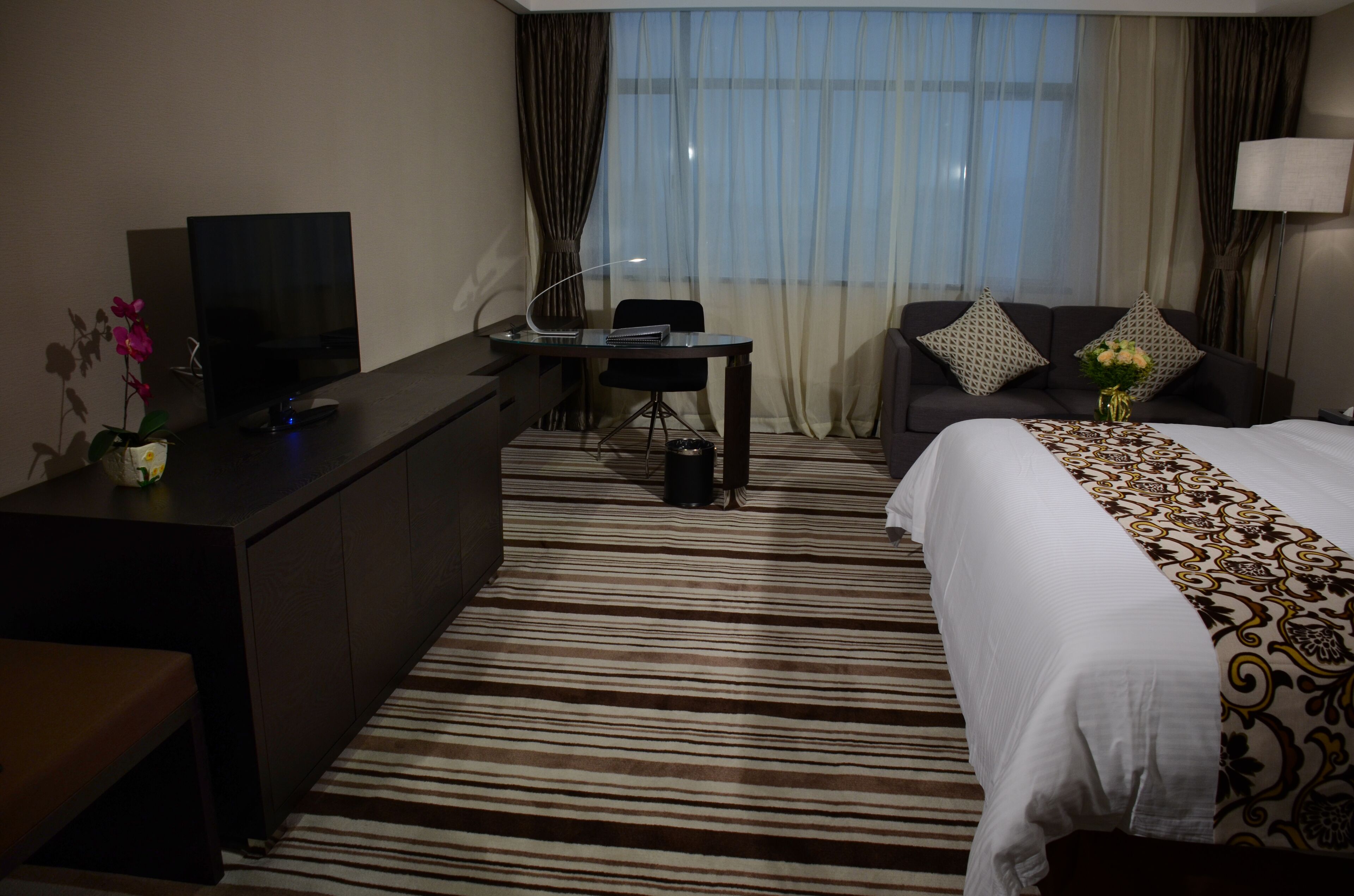 Una camera d'albergo con un letto, una scrivania, una televisione e una finestra con tende.