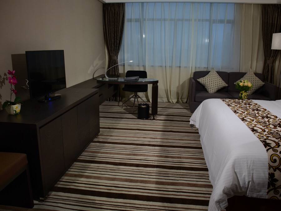 Una camera d'albergo con un letto, una scrivania, una televisione e una finestra con tende.