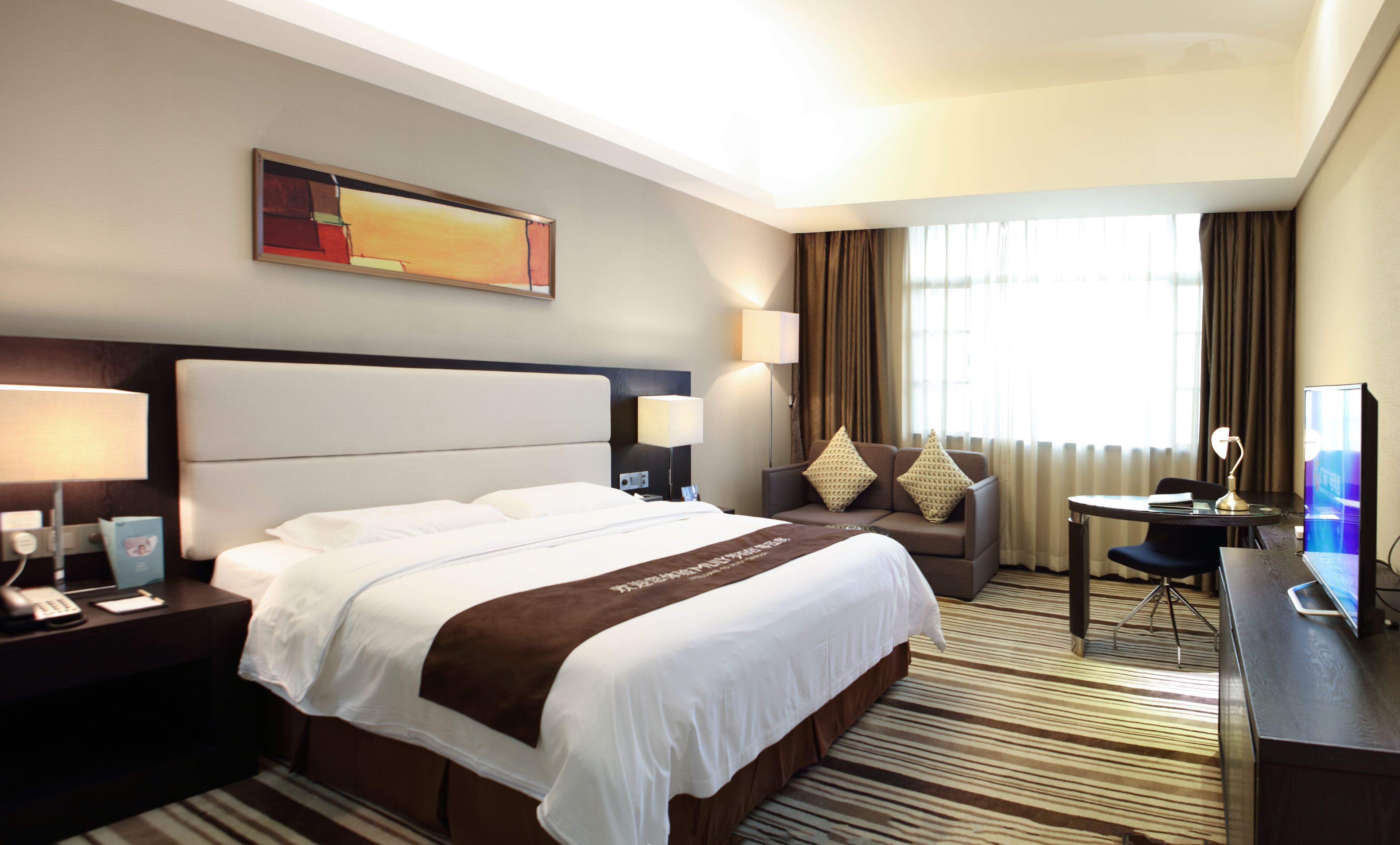 Habitación de hotel con una cama grande, un escritorio con computadora, una silla, una lámpara y un cuadro en la pared.