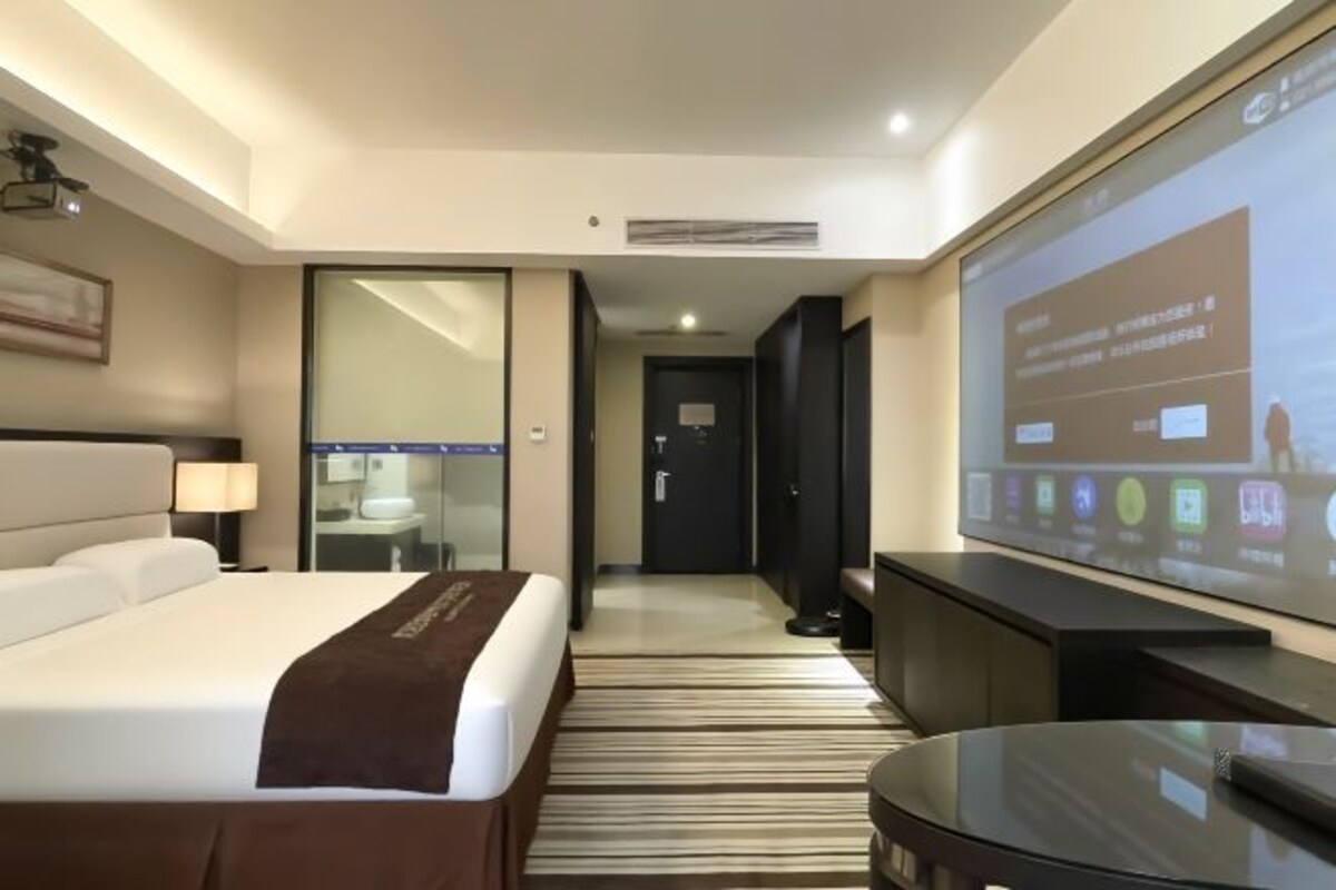 A hotel room with a bed, a desk, a television, and a large window.