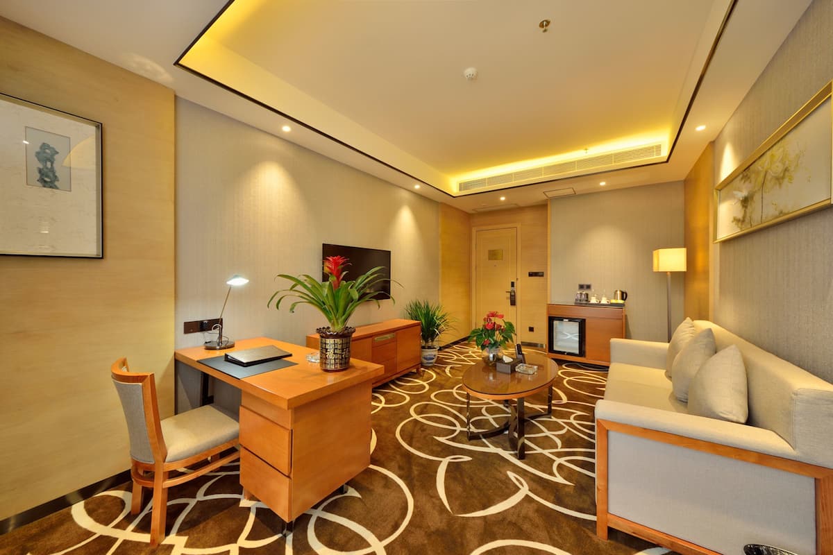 A hotel room with a wooden desk, a white sofa, a coffee table, and a TV.