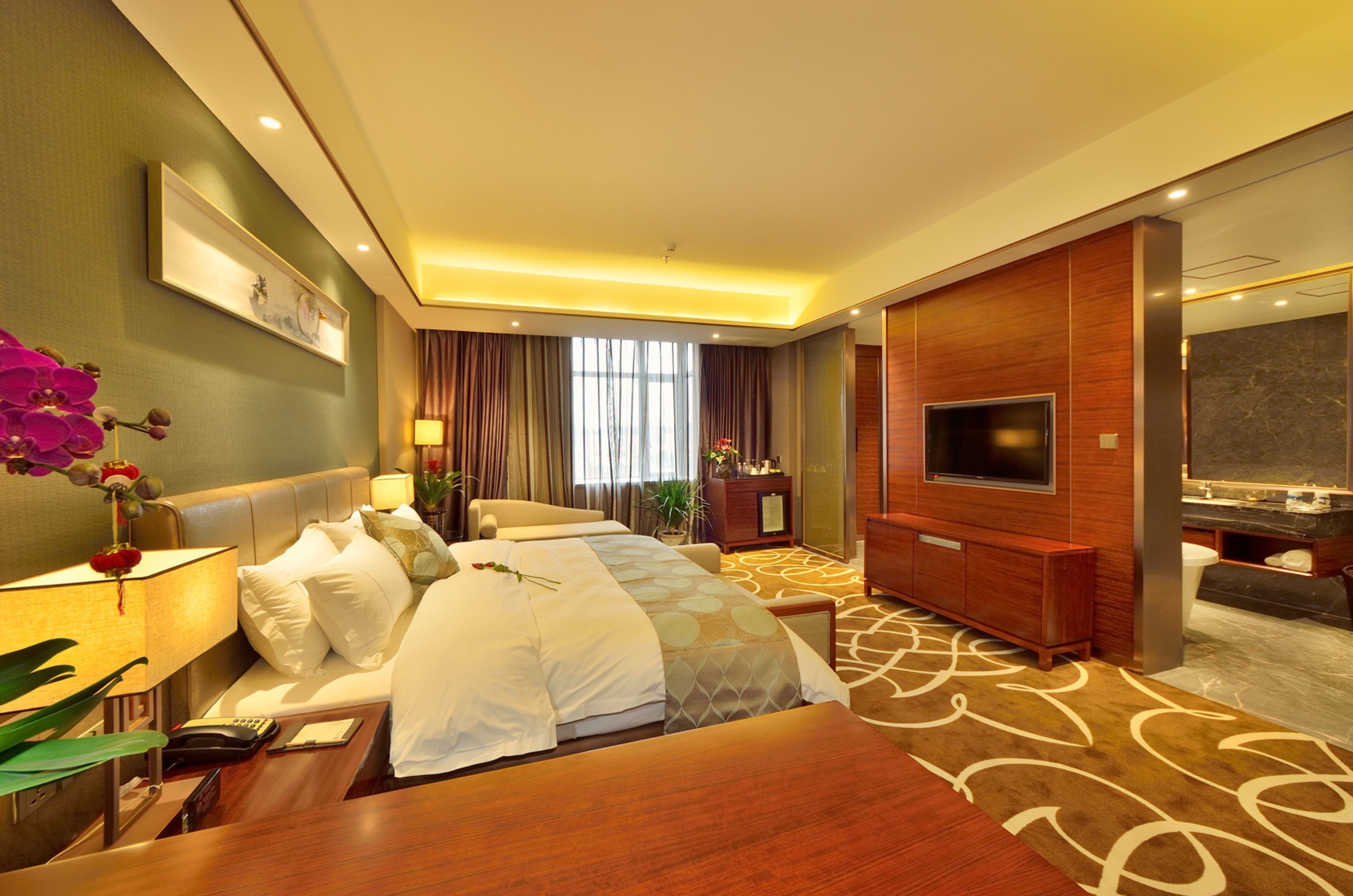 Quarto de hotel com uma cama grande, televisão, escrivaninha com abajur e banheiro com espelho e pia.