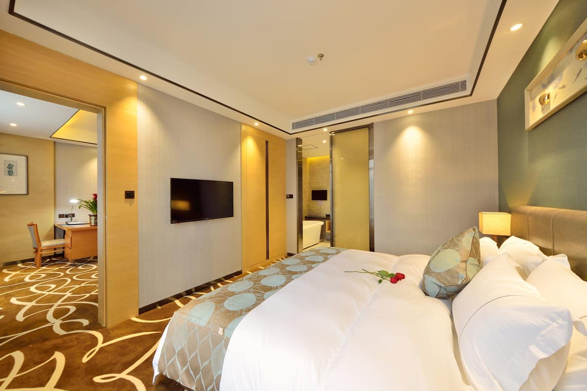 A hotel room with a large bed, a flat-screen TV, a desk with a chair, and a bathroom visible through an open door.