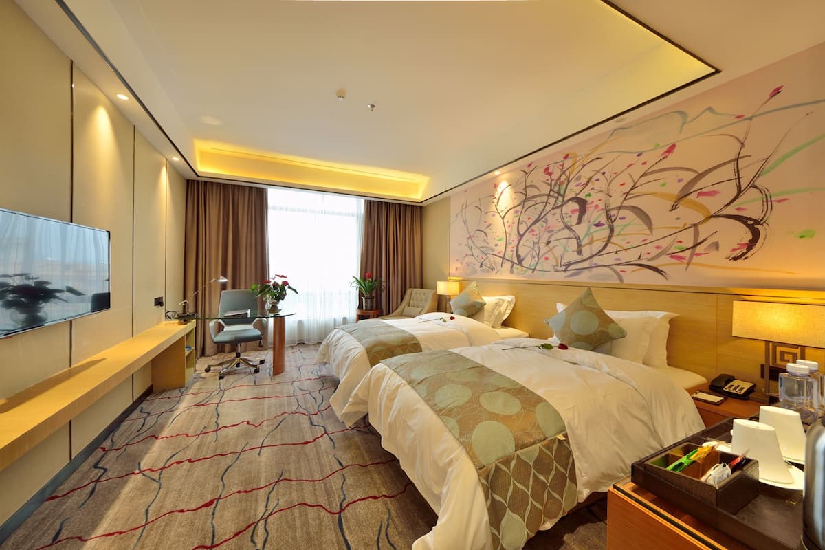 A hotel room with two beds, a desk, a TV, and a large abstract painting on the wall.