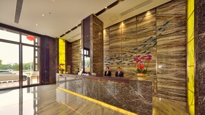 Een hotel receptie met een marmeren balie, grote ramen en decoratieve wandpanelen.