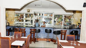 A bar area with multiple stools and a counter stocked with various bottles and glasses. - Paradise Hotel (Lomé)