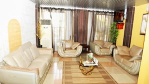 A living room with a beige sofa, two armchairs, a coffee table, and a television mounted on the wall. - Paradise Hotel (Lomé)