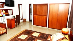 A bedroom with a bed, a desk, a chair, a wardrobe, a television, and a mirror. - Paradise Hotel (Lomé)