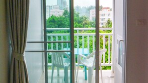 A room with a sliding glass door leading to a balcony with a view of buildings and greenery.