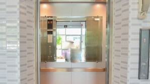 An elevator with a metallic interior, glass doors, and a control panel with an emergency button.
